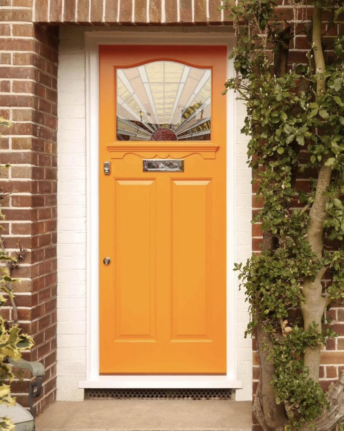 An orange-painted timber front door with a sunburst leaded panel, brick surround and ivy