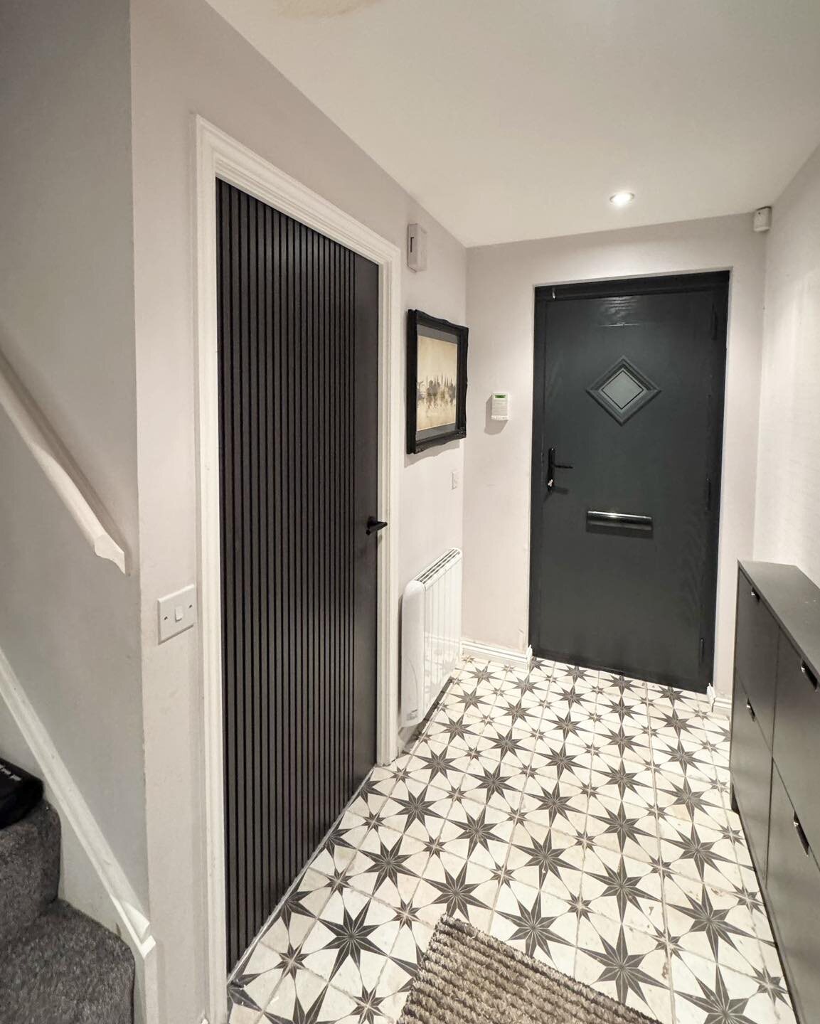 A black composite front door with a diamond glazed panel, seen from a hall with a star-patterned tiled floor