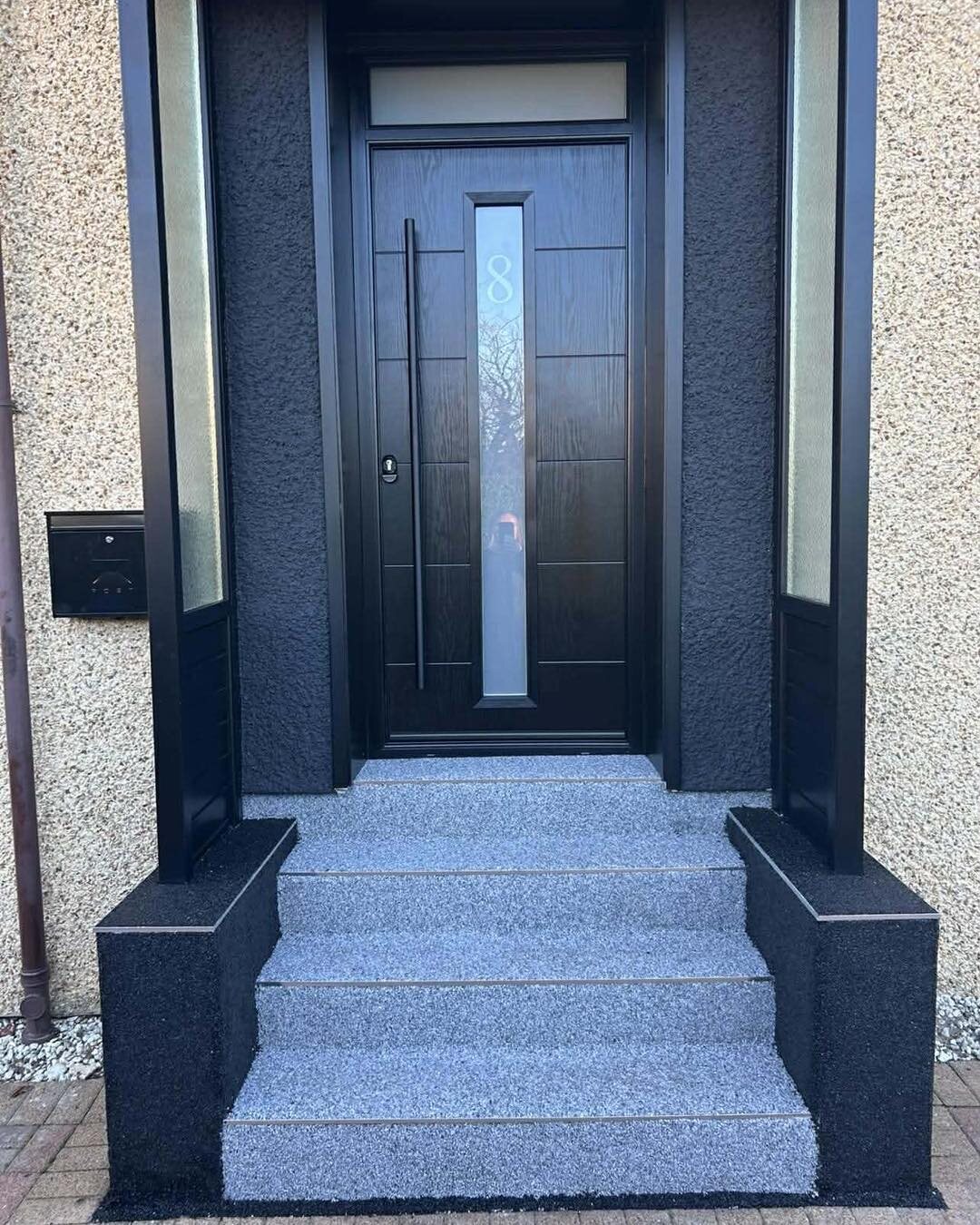 A black GRP composite front door with a slim glazed panel and side screens, above granite steps