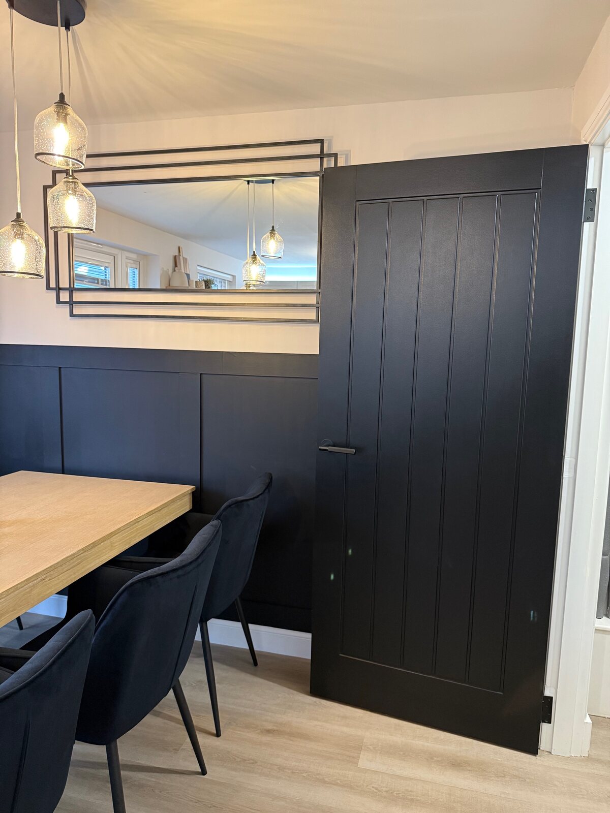 A black cottage door in a dining room with a navy panelled wall