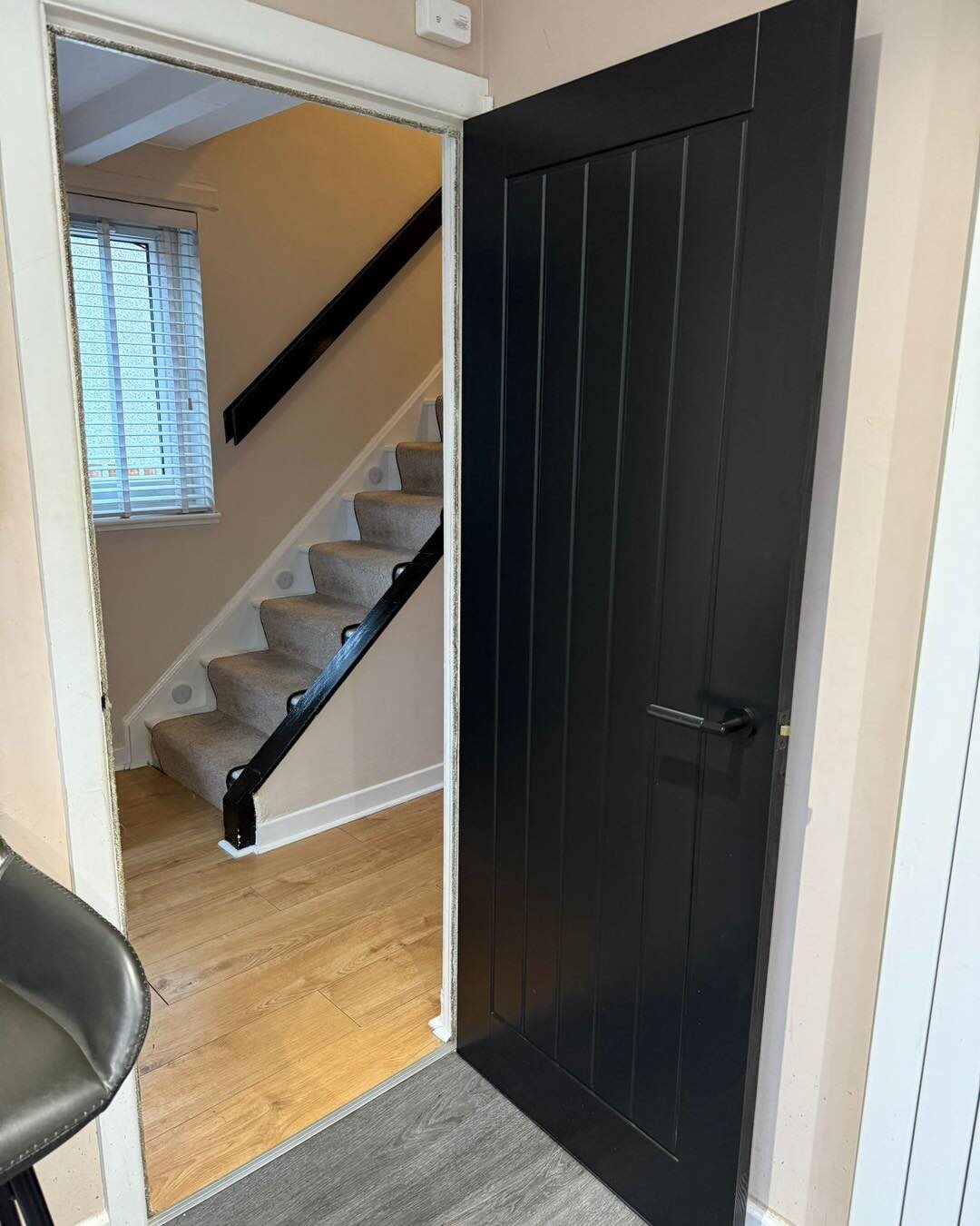 A black vertical-board cottage door at the foot of an open staircase