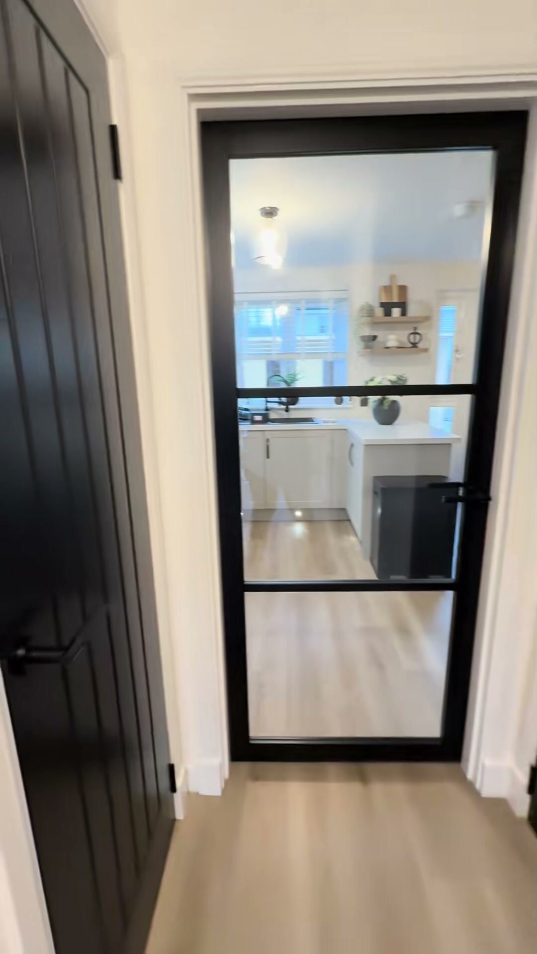 Still from our clip of a finished job: a black cottage door and black urban glazed doors through a hall into the kitchen