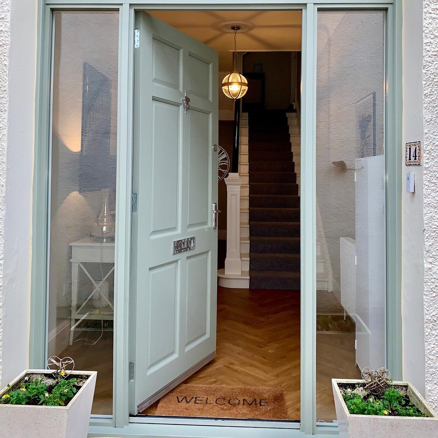 A sage timber front door and screen with glazed side panels, hand-finished, open onto a herringbone hall
