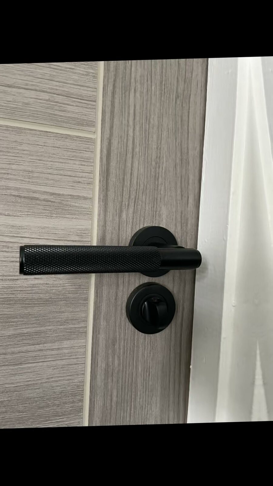 A black knurled handle on a white-grey Palermo door