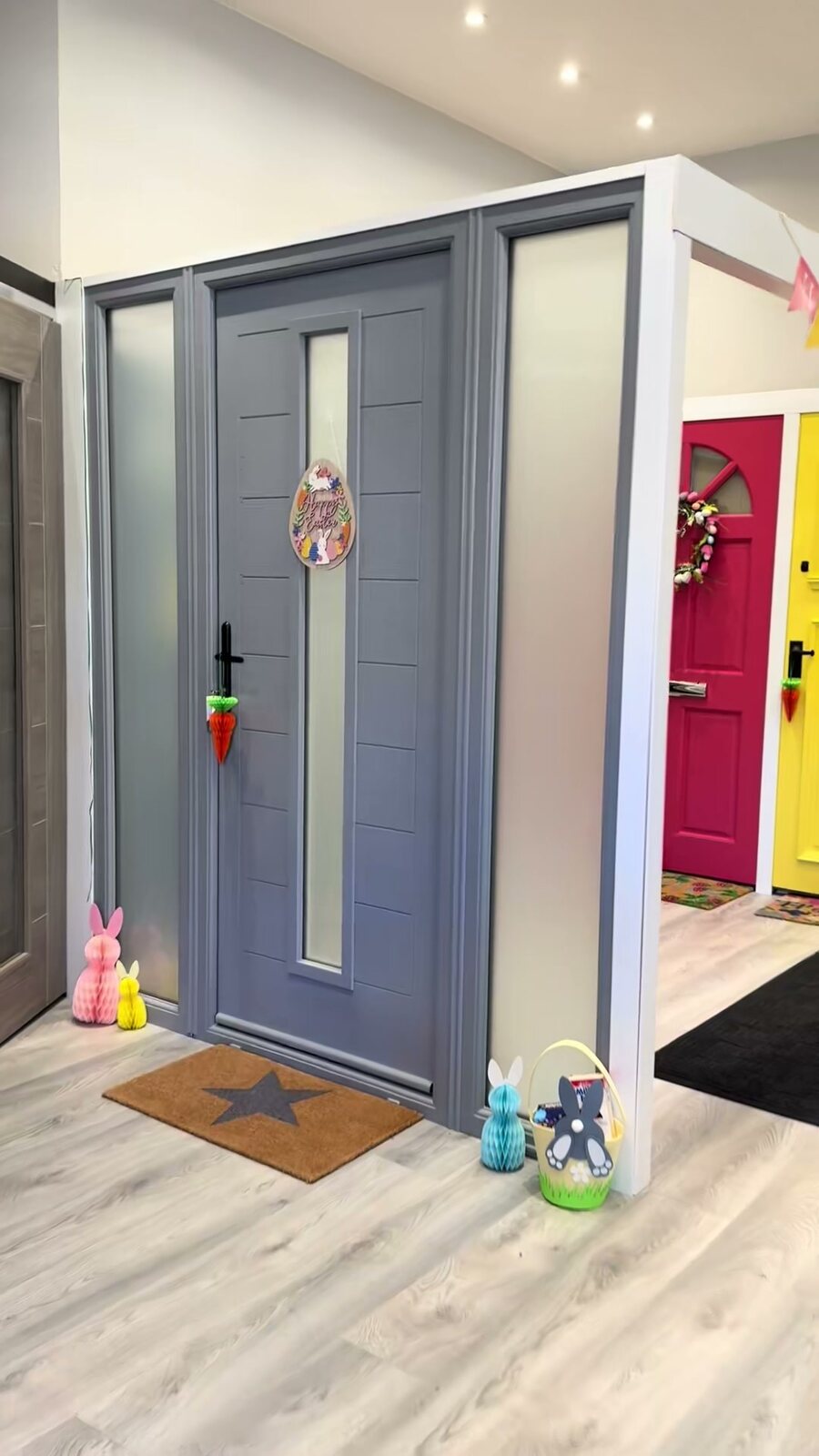A grey composite front door with glazed side screens on the showroom wall