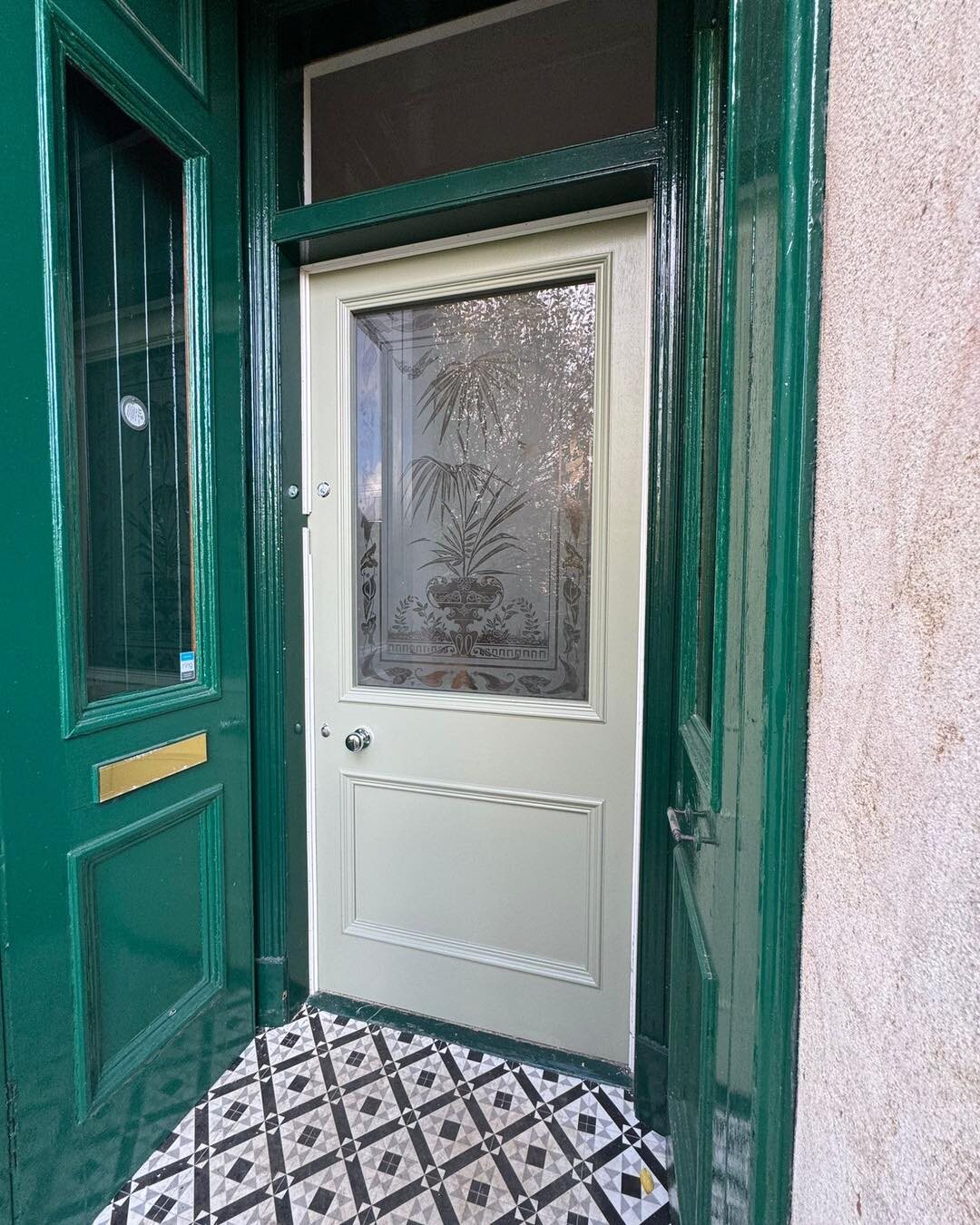 The new sage door with antique etched glass, behind green storm doors with a brass letterplate