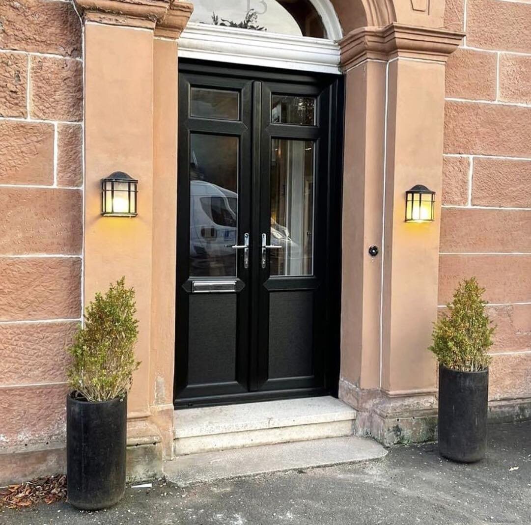 Black UPVC double storm doors on a red sandstone front, with carriage lamps