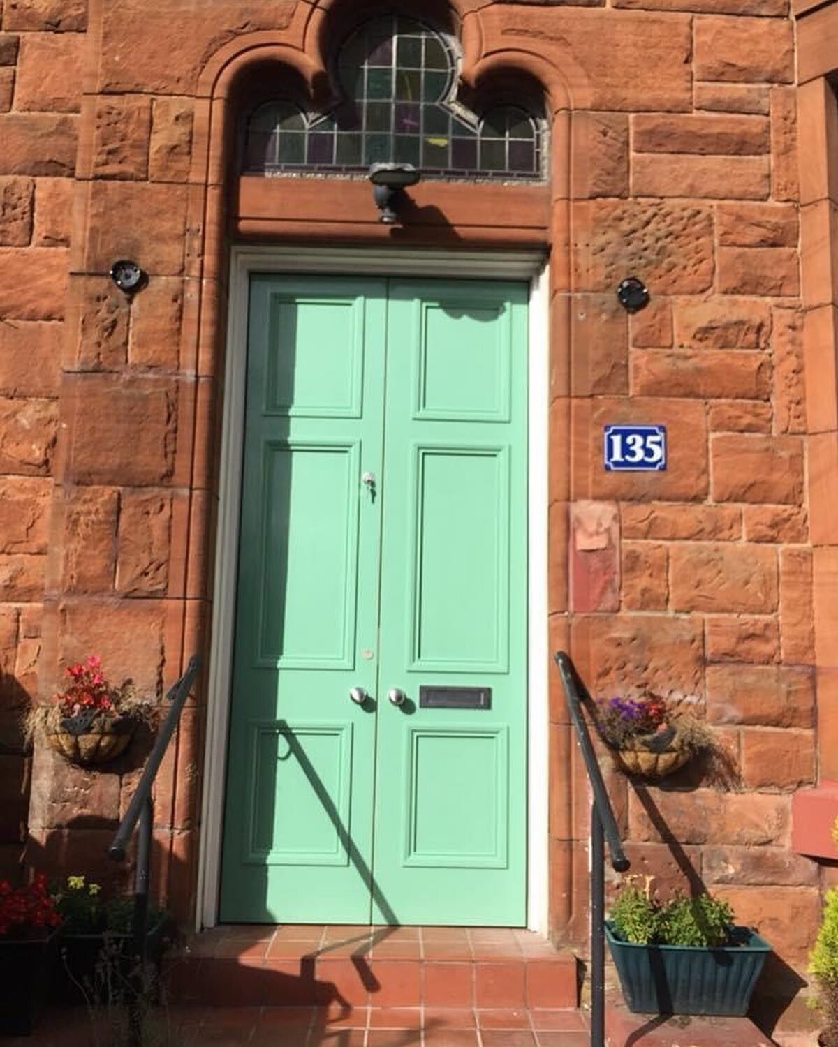 Mint-green hardwood storm doors in an arched red sandstone entrance