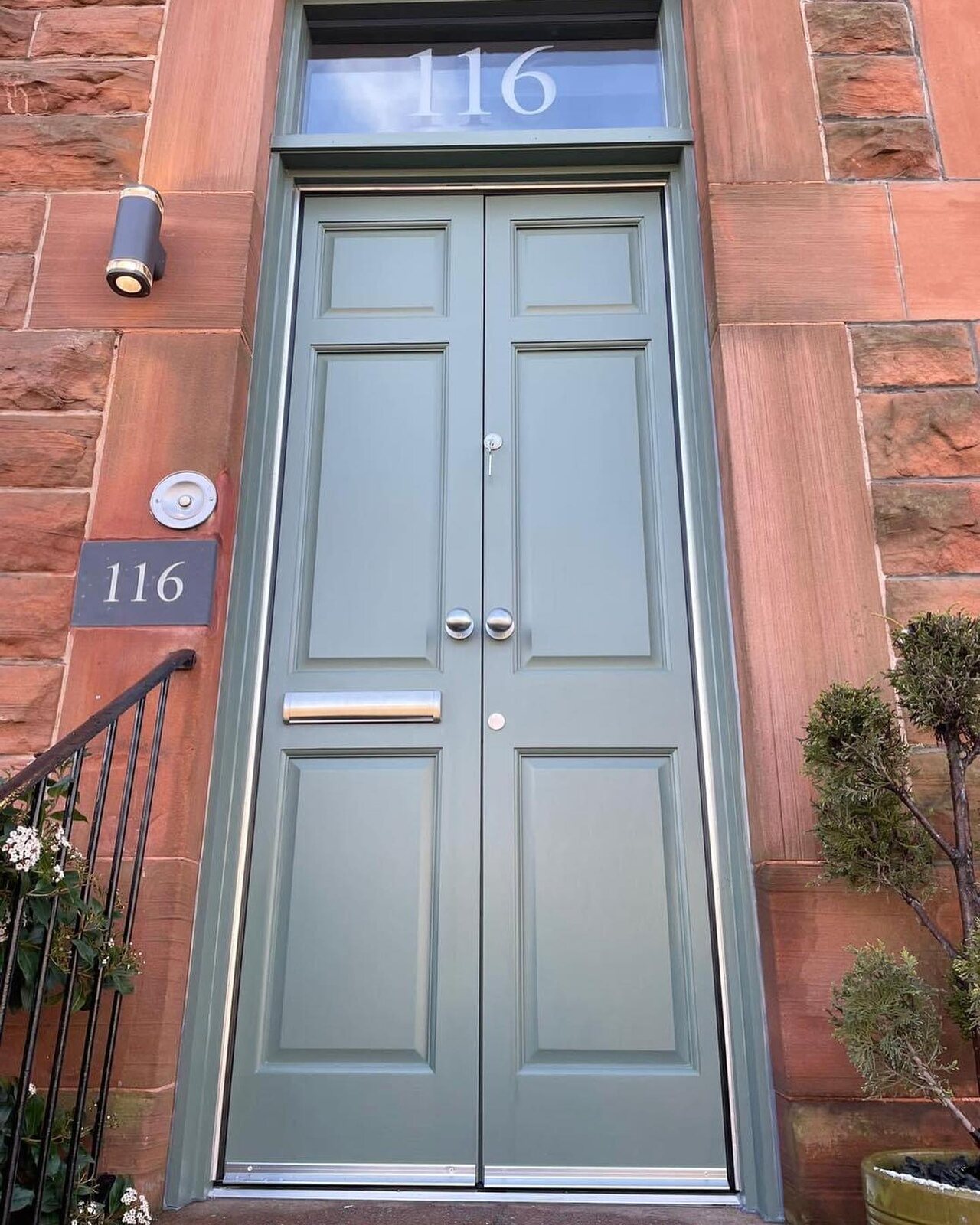 Grey-green hardwood double storm doors on a red sandstone front