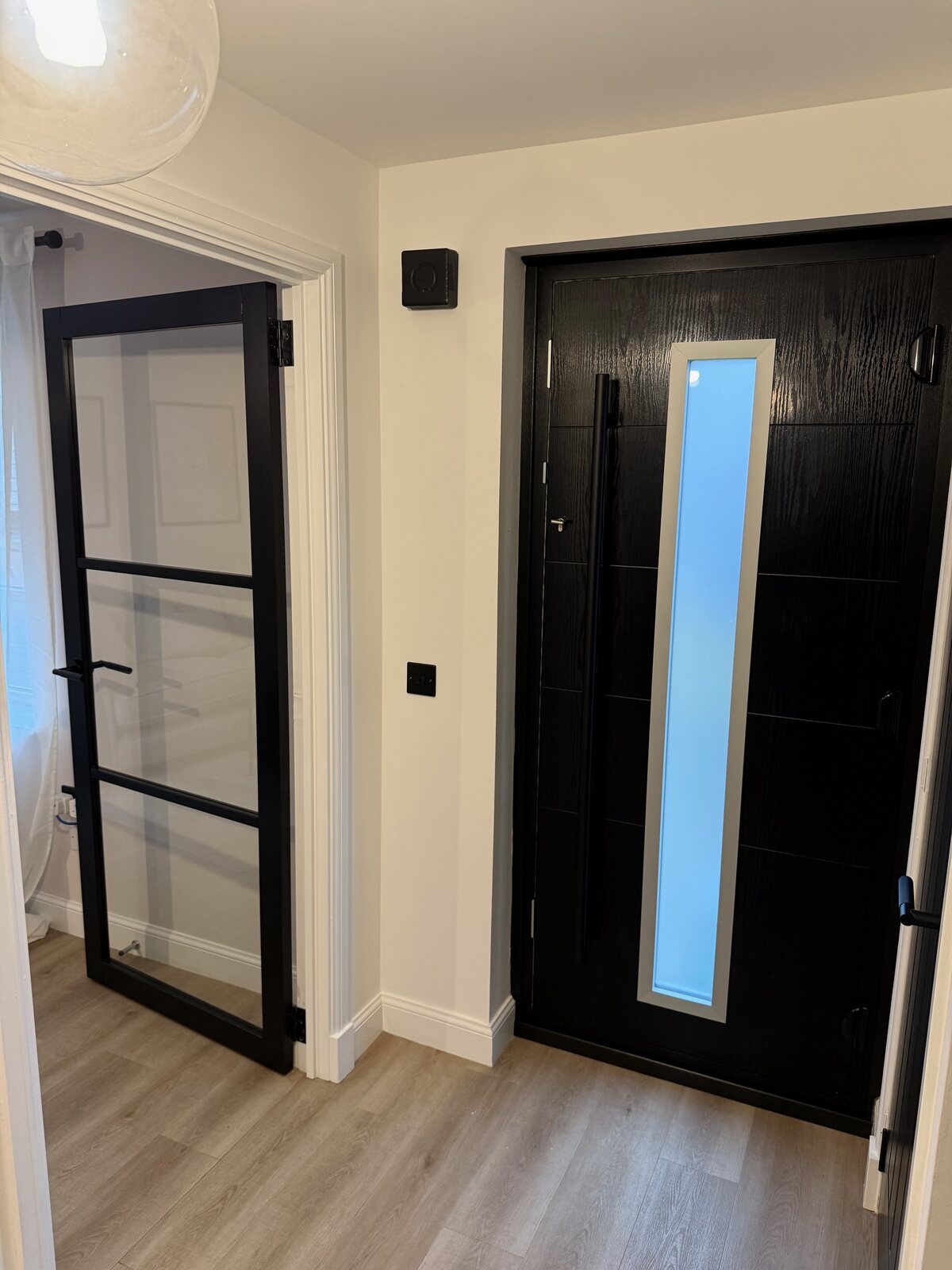 A black urban glazed door beside a black front door with a tall glazed panel
