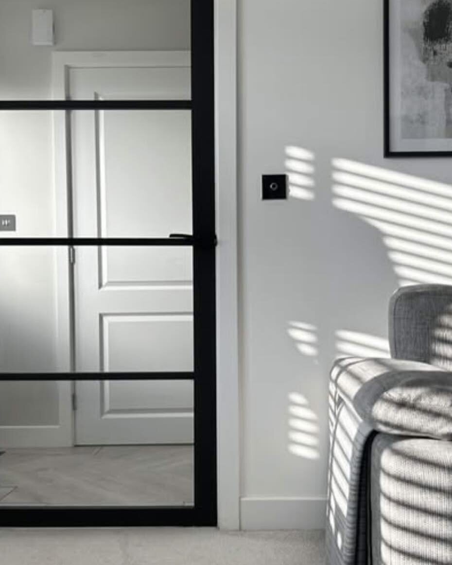 A black urban glazed divider in a white living room, with striped sunlight across it