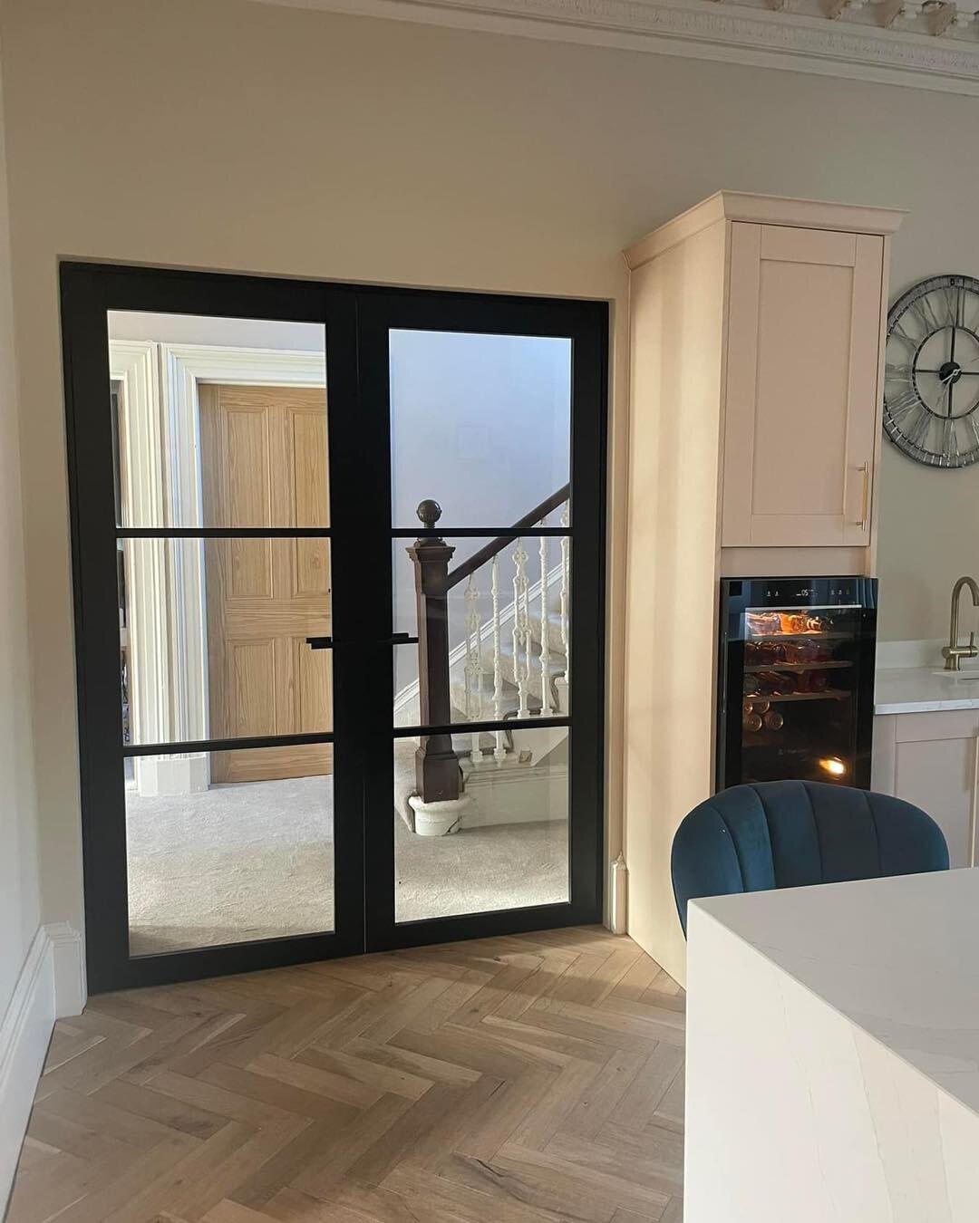 Black urban glazed French doors into an open kitchen with a herringbone floor