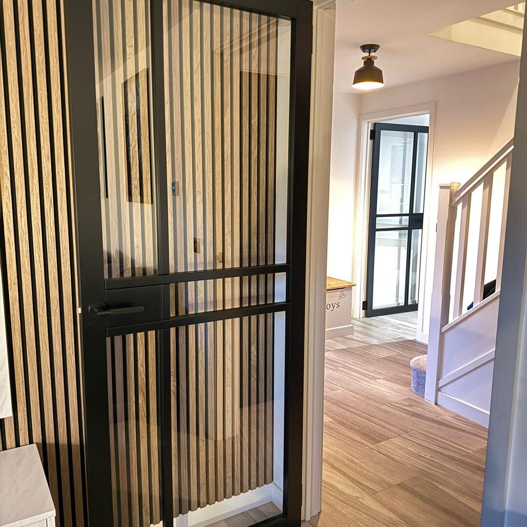 Two black urban glazed doors in line down a hall, black slatted wall panel, oak floor