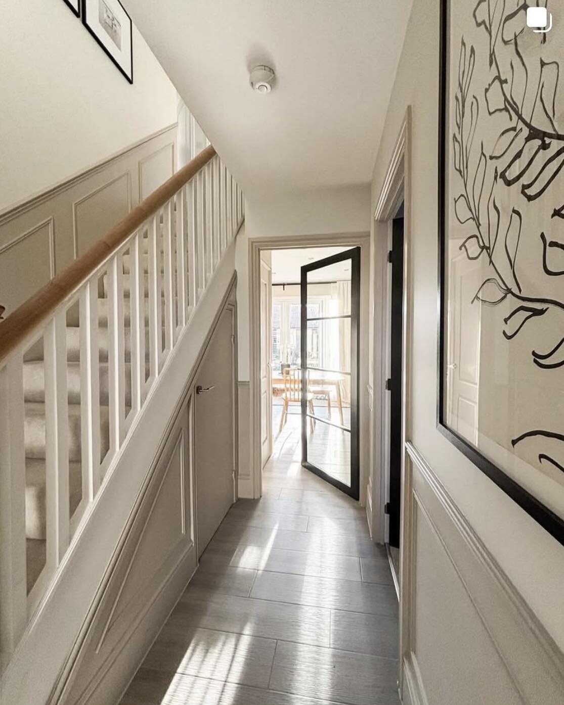 A hall beneath a white spindle staircase, a black urban glazed door at the far end