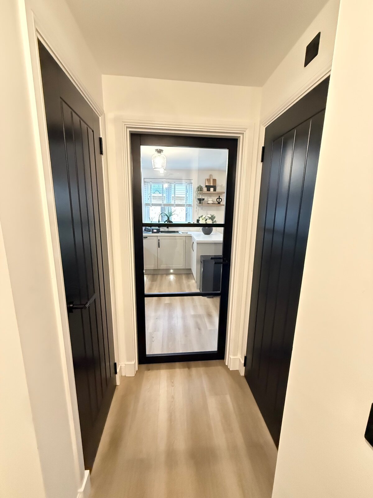 Looking through a black urban glazed door into a kitchen, a black cottage door on the right