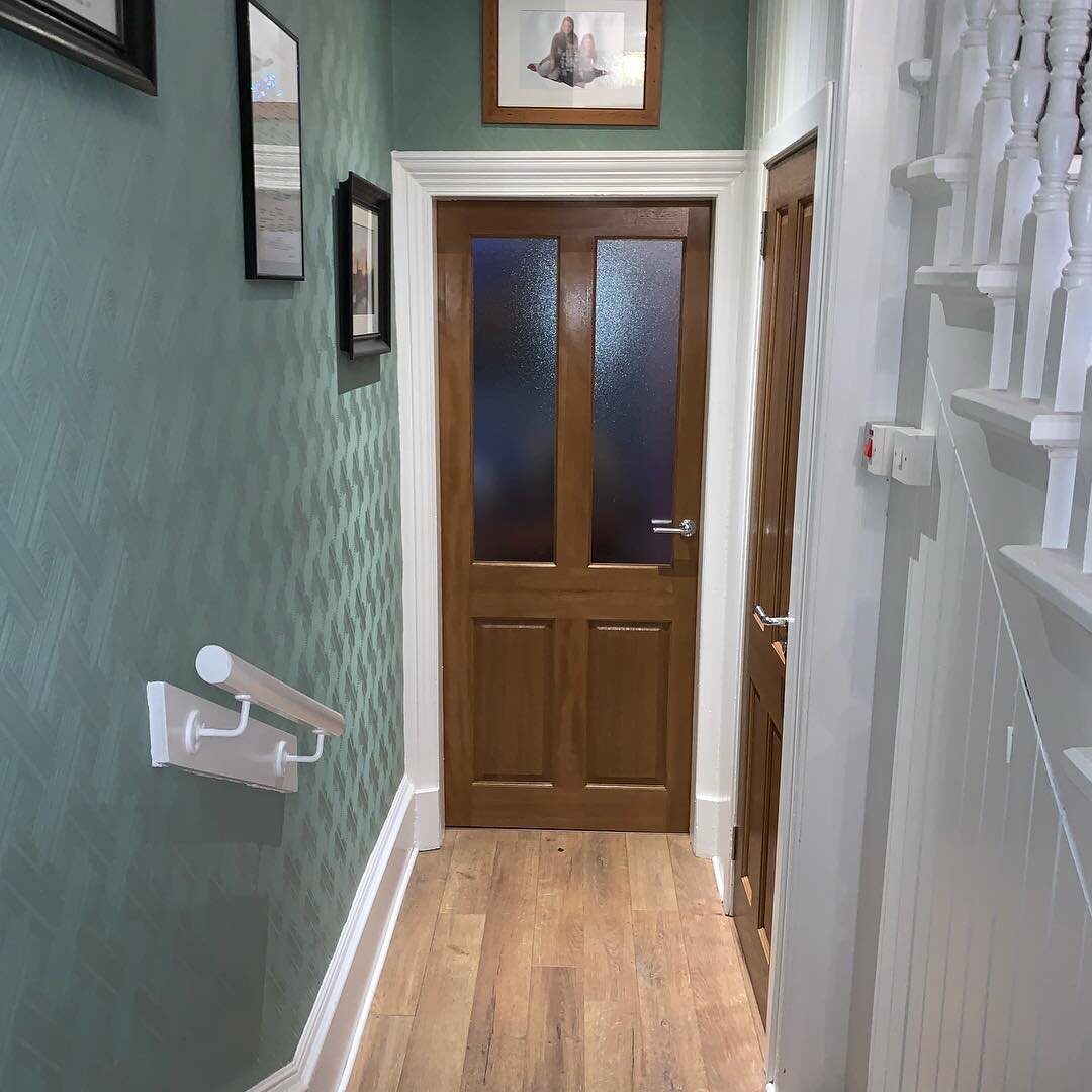 A hardwood four-panel glazed internal door at the end of a sage hall