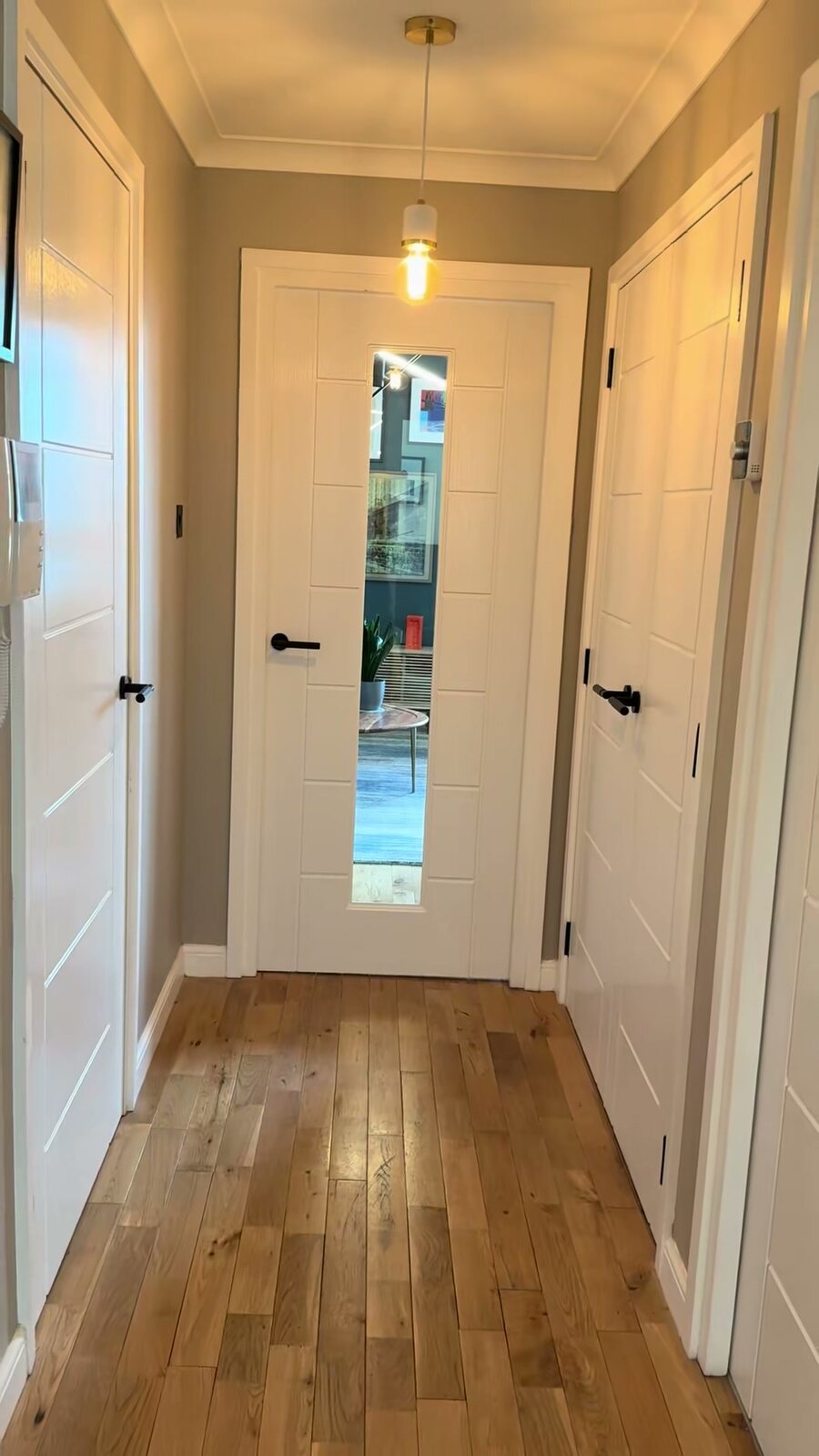 White no-more-paint doors down a hall with an oak floor and black handles